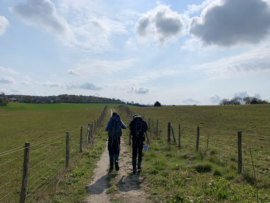 Two D of E students with large backpacks walk along a track between fields in beautiful sunshine
