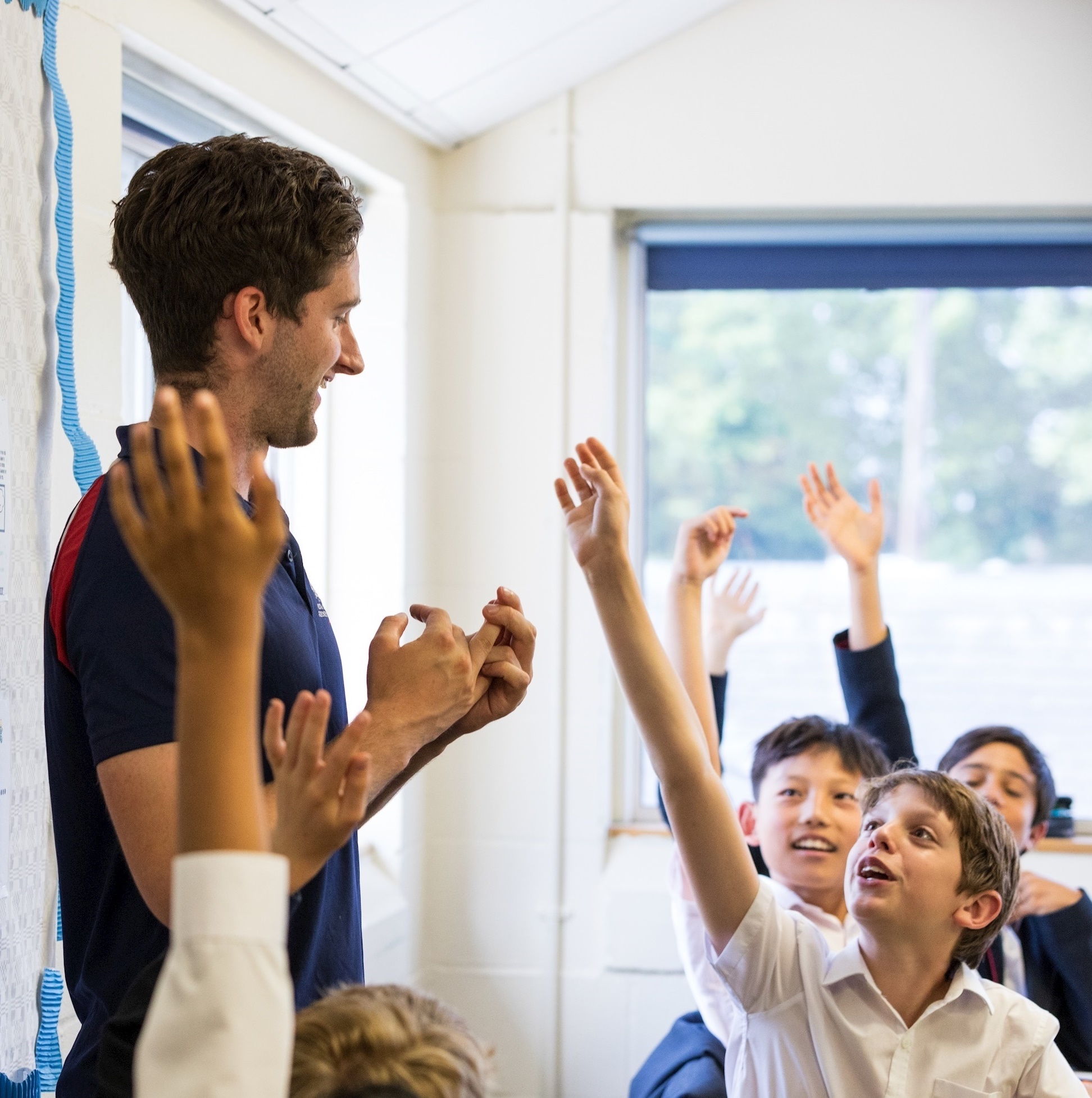 Image of male teacher with lots of hands up in the class